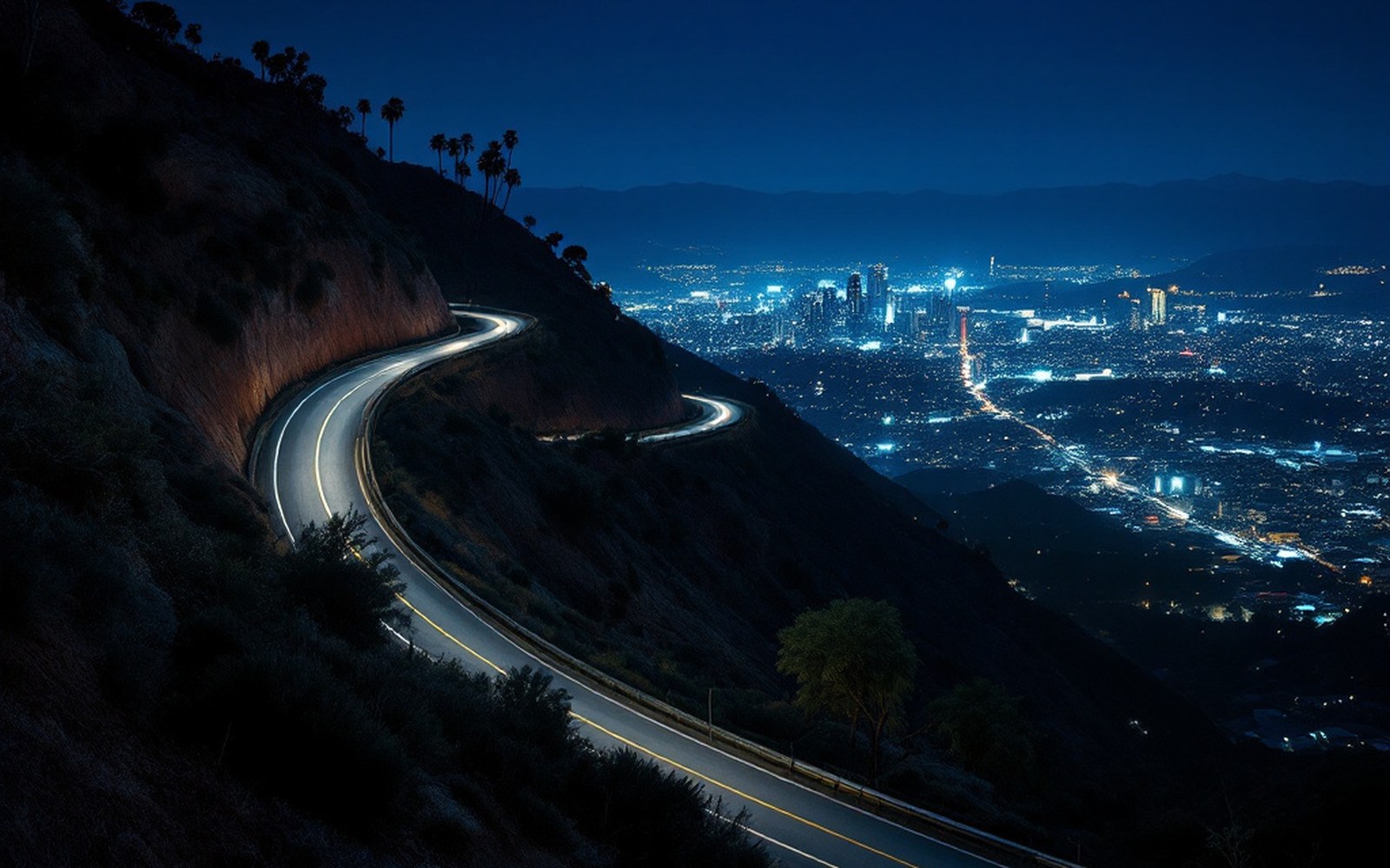 Mulholland Drive itself at night: a two-lane road curving along a ridge above the lights of the basin, headlights climbing, no cars parked